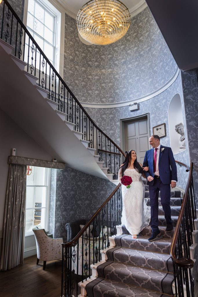 Father of the Bride walking his daughter down the grand staircase to the wedding ceremony room at the De Vere Beaumont Estate in Windsor. 